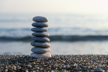 Balanced pebble pyramid silhouette on the beach with the ocean in the background. Zen stones on the sea beach, meditation, spa, harmony, calmness, balance concept.	