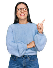 Young hispanic woman wearing casual clothes and glasses with a big smile on face, pointing with hand and finger to the side looking at the camera.