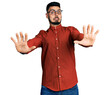 © Krakenimages.com - Young hispanic man with beard wearing business shirt and glasses afraid and terrified with fear expression stop gesture with hands, shouting in shock. panic concept.