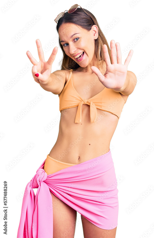Beautiful brunette young woman wearing bikini and sunglasses showing and pointing up with fingers number eight while smiling confident and happy.