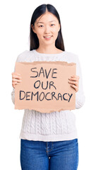 Poster - Young beautiful chinese woman holding save our democracy cardboard banner looking positive and happy standing and smiling with a confident smile showing teeth