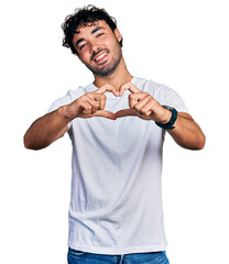 Wall Mural - Hispanic young man with beard wearing casual white t shirt smiling in love doing heart symbol shape with hands. romantic concept.