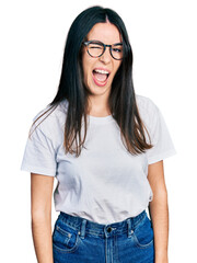 Wall Mural - Young hispanic woman wearing casual clothes and glasses winking looking at the camera with sexy expression, cheerful and happy face.