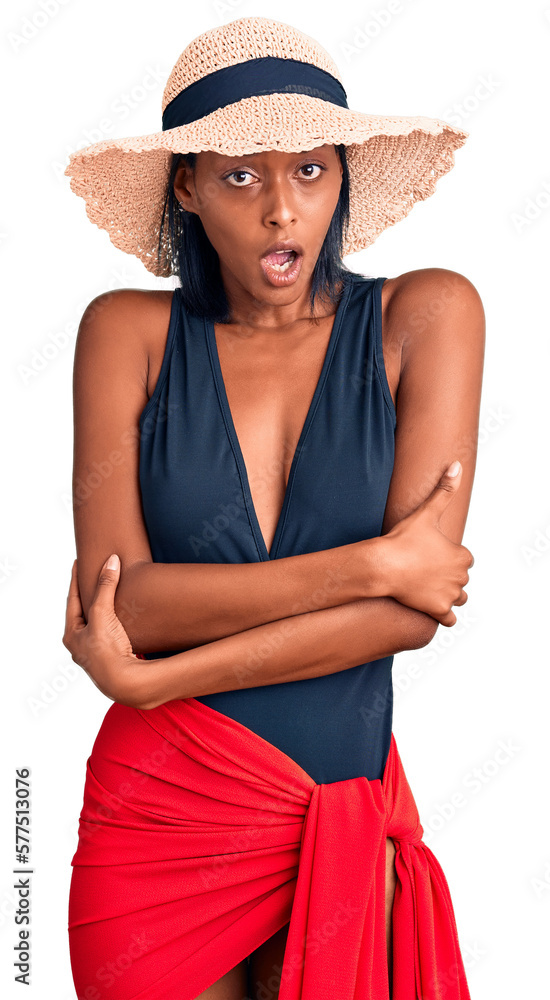 Young african american woman wearing swimsuit and summer hat shaking and freezing for winter cold with sad and shock expression on face