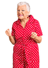 Wall Mural - Senior beautiful woman with blue eyes and grey hair wearing a red summer dress very happy and excited doing winner gesture with arms raised, smiling and screaming for success. celebration concept.