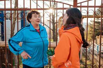 Concept of the International Day of Older Persons. A happy grandmother and granddaughter communicate standing on the street. A fence and sunset light in the background