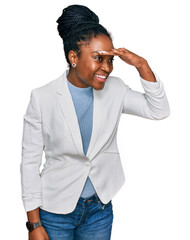 Sticker - Young african american woman wearing business clothes very happy and smiling looking far away with hand over head. searching concept.