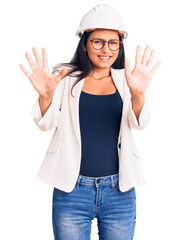 Poster - Young beautiful latin girl wearing architect hardhat and glasses afraid and terrified with fear expression stop gesture with hands, shouting in shock. panic concept.