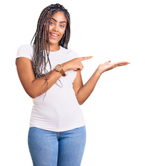 Sticker - Young african american woman with braids wearing casual clothes amazed and smiling to the camera while presenting with hand and pointing with finger.