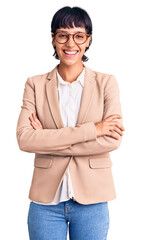 Young brunette woman with short hair wearing business jacket and glasses happy face smiling with crossed arms looking at the camera. positive person.