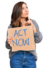 Poster - Young brunette woman holding act now banner serious face thinking about question with hand on chin, thoughtful about confusing idea