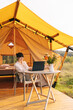 © Ananass - young woman working on a laptop while sitting near a big tent in nature