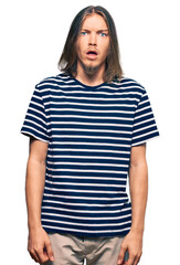 Poster - Handsome caucasian man with long hair wearing casual striped t-shirt afraid and shocked with surprise expression, fear and excited face.