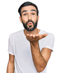 Wall Mural - Young hispanic man wearing casual white t shirt looking at the camera blowing a kiss with hand on air being lovely and sexy. love expression.