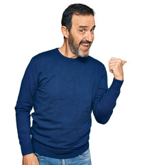 Canvas Print - Middle age hispanic man wearing casual clothes smiling with happy face looking and pointing to the side with thumb up.