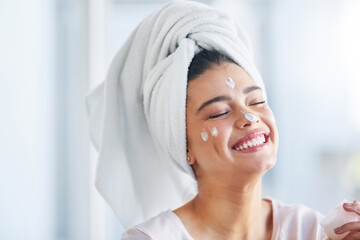 Wall Mural - Not a wrinkle in sight. Shot of a beautiful young woman applying moisturizer to her skin in the bathroom at home.