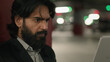 © Yuliia - Close-up puzzled serious Indian man looking at laptop screen in underground parking focused worried young arabian businessman feeling anxiety from reading bad business news working remote on Internet