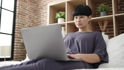 Poster - Young chinese woman using laptop sitting on bed at bedroom