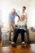 © A.B./peopleimages.com - Surrounded by support. Shot of a smiling caregiver with a senior woman in a wheelchair and her husband at home.
