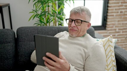 Sticker - Middle age grey-haired man using touchpad sitting on sofa at home