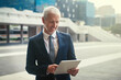 © Adene S/peopleimages.com - Im loving my new gadget. Shot of a confident businessman using his tablet while standing outside his office building.