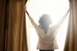 © Lyndon S/peopleimages.com - New day, new possibilities. Rearview shot of a woman opening the curtains on a bright sunny day.