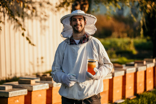 young experienced beekeeper in protective workwear working at apiary and feeding hives. he is happy 