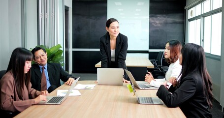 Asian boss business woman standing to talking with team on meeting around board table at office