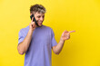 © luismolinero - Young caucasian man using mobile phone isolated on yellow background pointing finger to the side and presenting a product