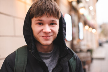 Funny smiling teenage boy 17-18 year old with blond hair wearing hoodie walking in city street outdoor. Looking at camera. Teenagerhood.