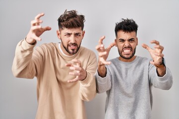 Wall Mural - Young homosexual couple standing over white background shouting frustrated with rage, hands trying to strangle, yelling mad