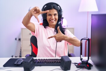 Sticker - Mature hispanic woman playing video games at home smiling making frame with hands and fingers with happy face. creativity and photography concept.