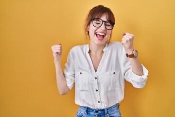 Sticker - Young beautiful woman wearing casual shirt over yellow background celebrating surprised and amazed for success with arms raised and eyes closed. winner concept.