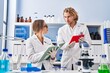 © Krakenimages.com - Man and woman wearing scientist uniform writing on notebook using touchpad at laboratory