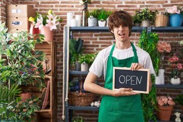 Sticker - Hispanic young man working at florist holding open sign clueless and confused expression. doubt concept.