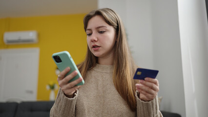 Wall Mural - Young blonde woman using smartphone and credit card sitting on floor at home