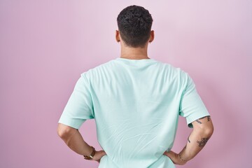 Wall Mural - Handsome hispanic man standing over pink background standing backwards looking away with arms on body