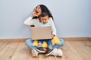 Poster - Young hispanic mother and kid using computer laptop sitting on the floor shouting and screaming loud to side with hand on mouth. communication concept.