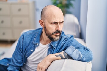 Sticker - Young bald man sitting on sofa with serious expression at home