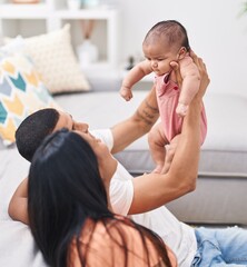 Poster - Hispanic family holding baby on air sitting on floor at home