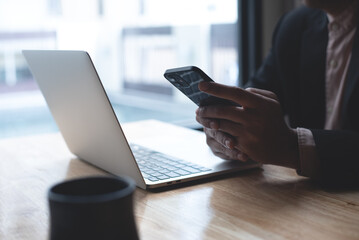 Businessman using mobile smart phone texting to colleague during working on laptop computer at office. Man manager sitting at table surfing the internet