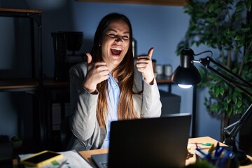 Canvas Print - Young brunette woman working at the office at night success sign doing positive gesture with hand, thumbs up smiling and happy. cheerful expression and winner gesture.