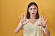© Krakenimages.com - Hispanic girl wearing casual t shirt over yellow background doing stop gesture with hands palms, angry and frustration expression