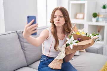 Canvas Print - Caucasian woman holding bouquet of white flowers taking a selfie picture puffing cheeks with funny face. mouth inflated with air, catching air.