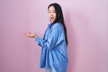 Sticker - Young asian woman standing over pink background pointing aside with hands open palms showing copy space, presenting advertisement smiling excited happy