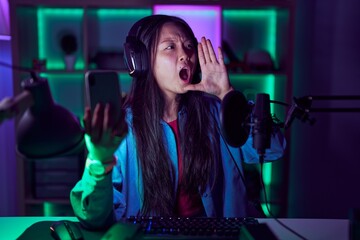 Canvas Print - Young asian woman playing video games with smartphone shouting and screaming loud to side with hand on mouth. communication concept.