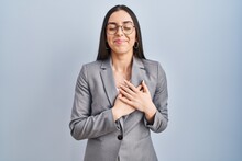 Hispanic Business Woman Wearing Glasses Smiling With Hands On Chest With Closed Eyes And Grateful Gesture On Face. Health Concept.