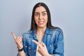 Sticker - Hispanic woman standing over blue background pointing aside worried and nervous with both hands, concerned and surprised expression