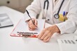 © Krakenimages.com - Middle age woman wearing doctor uniform writing on paperwork at clinic