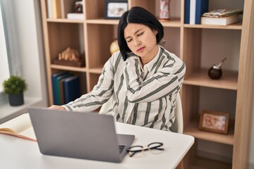 Wall Mural - Young chinese woman studying sitting on table suffering for backache at home